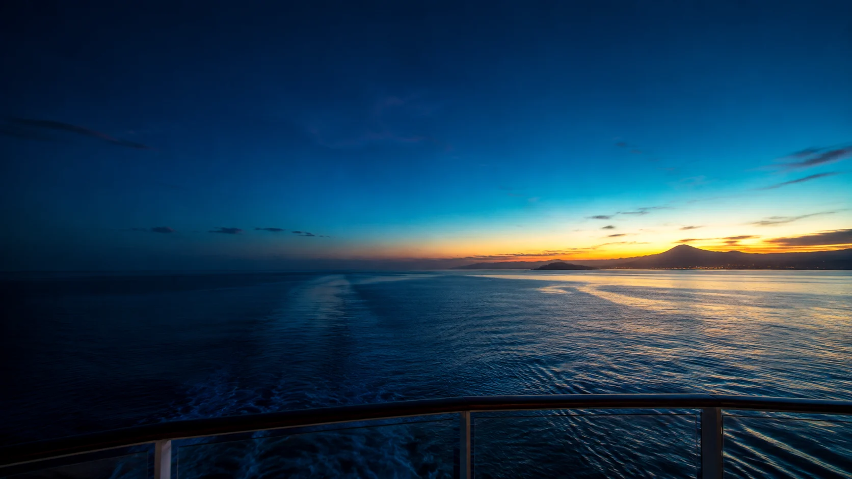 Twilight over the open sea, seen past the railing at the back of a cruise ship
